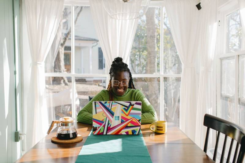 a woman smiling at her laptop screen in the dining area